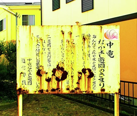 Severe rust patches interrupt columns of Japanese lettering on a yellow roadside sign.