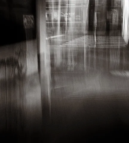 Vertical architectural lines dissolve into pale streaks above deep shadow in a blurred black and white scene.