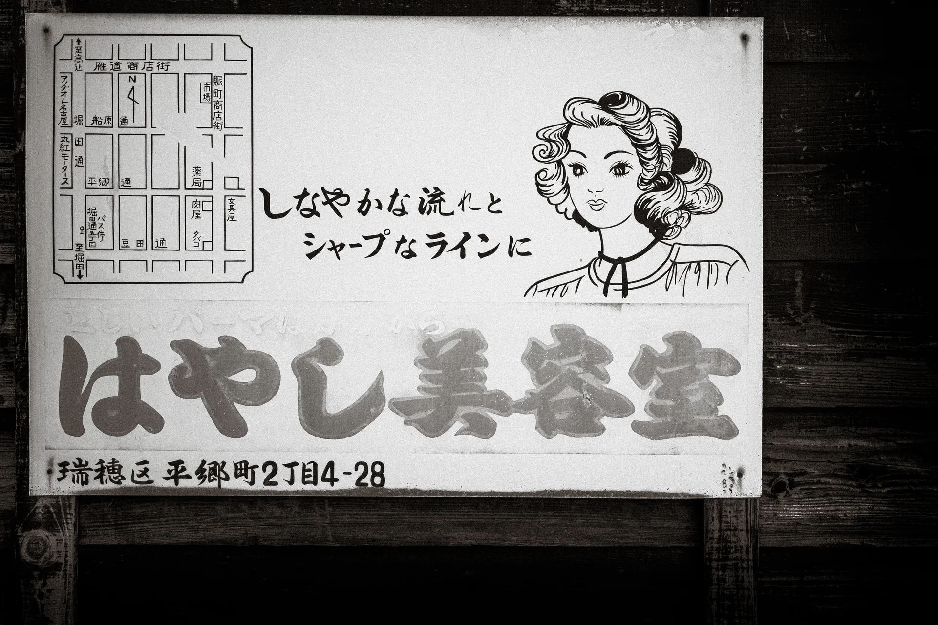 An illustrated woman's face and Japanese lettering fill a weathered rectangular sign in black and white.