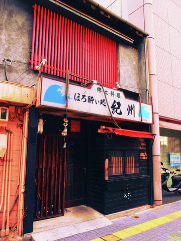 A dark restaurant entrance sits below a pale sign and bright red vertical upper-window slats.