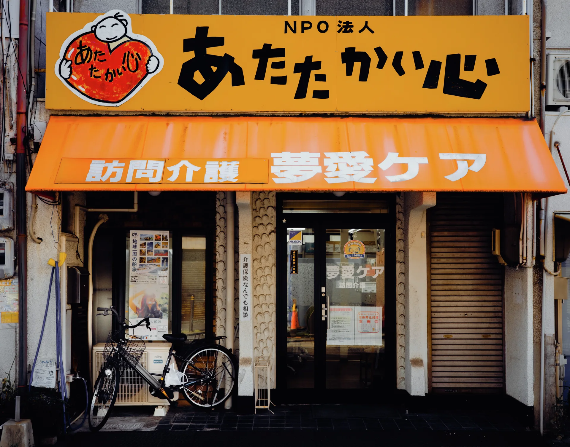 An orange sign and matching awning cover a glass entrance with a bicycle parked beside it.