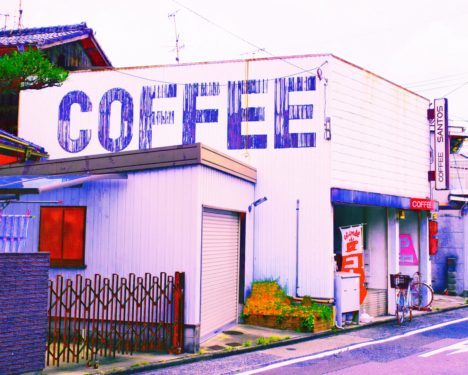 Huge blue COFFEE letters cover a pale corner building beside closed shutters and a narrow entrance.