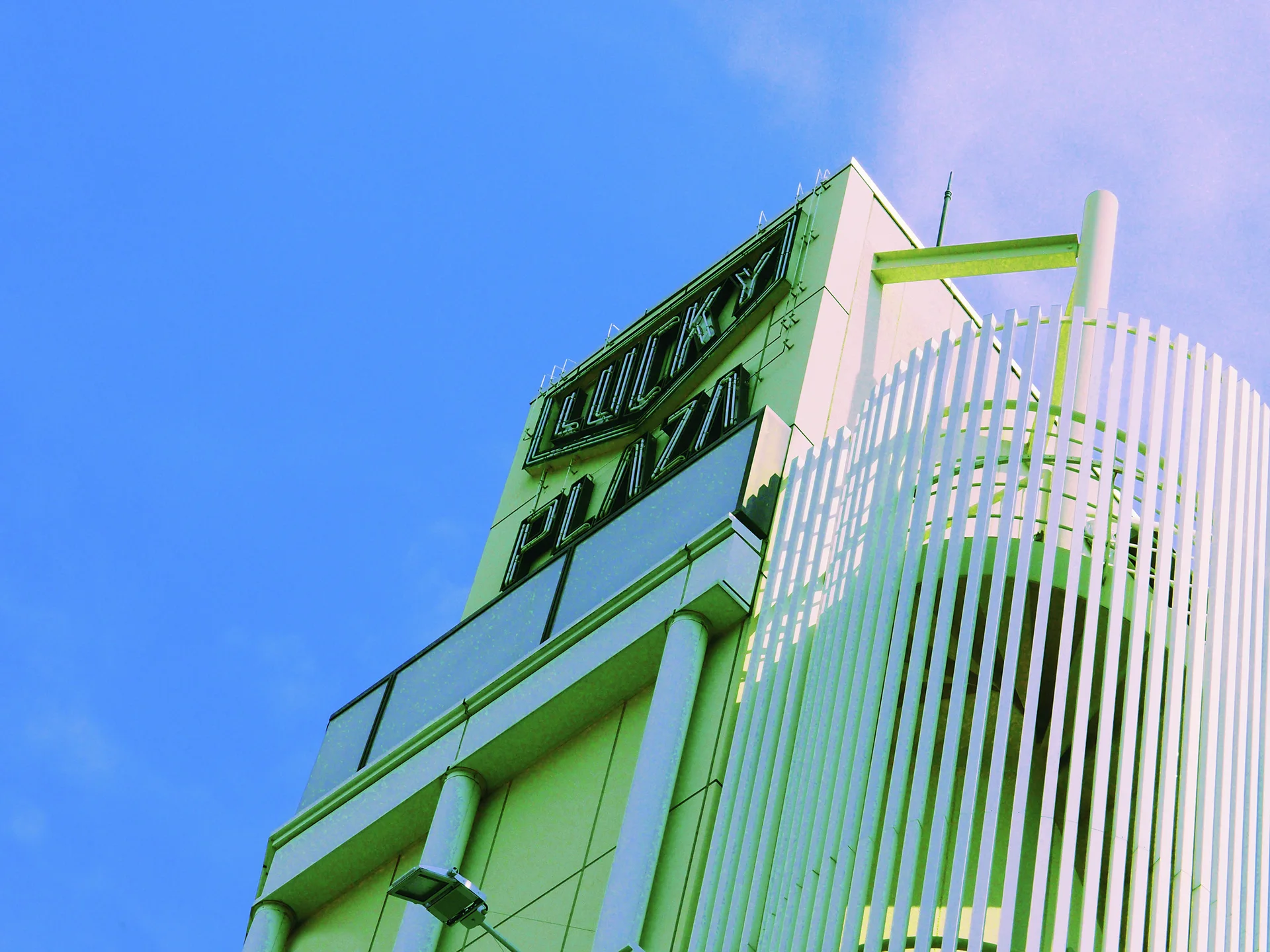 Tall white curved slats rise beside a pale building with dark windows beneath blue sky.