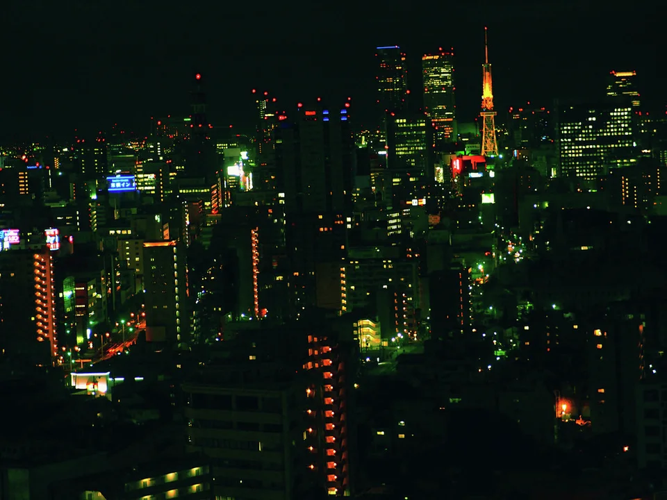 An orange-lit tower rises among dark skyscrapers and scattered green and white city lights.