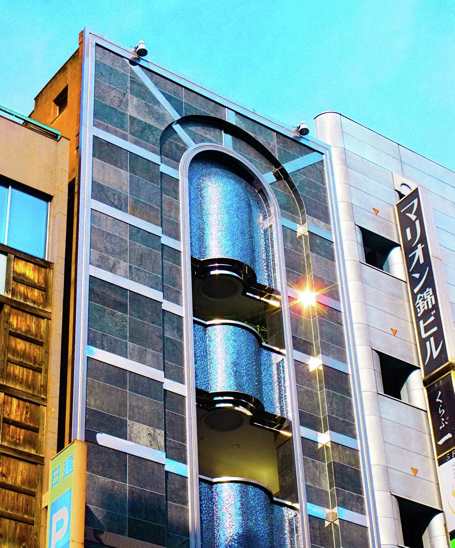 Three curved blue balconies fill a tall arched recess in a gray building beneath turquoise sky.