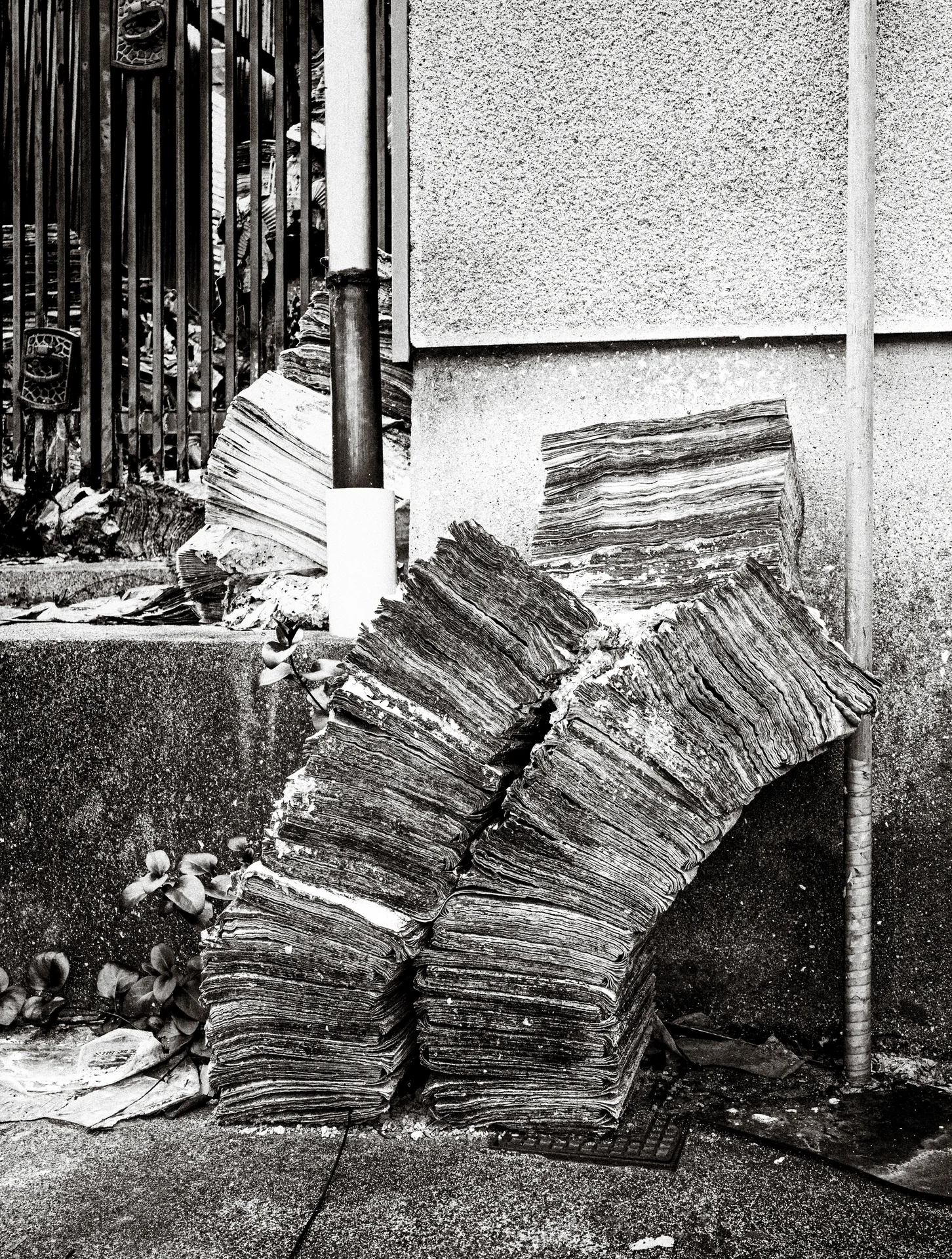 Tall uneven stacks of thin boards lean against a rough exterior wall in black and white.