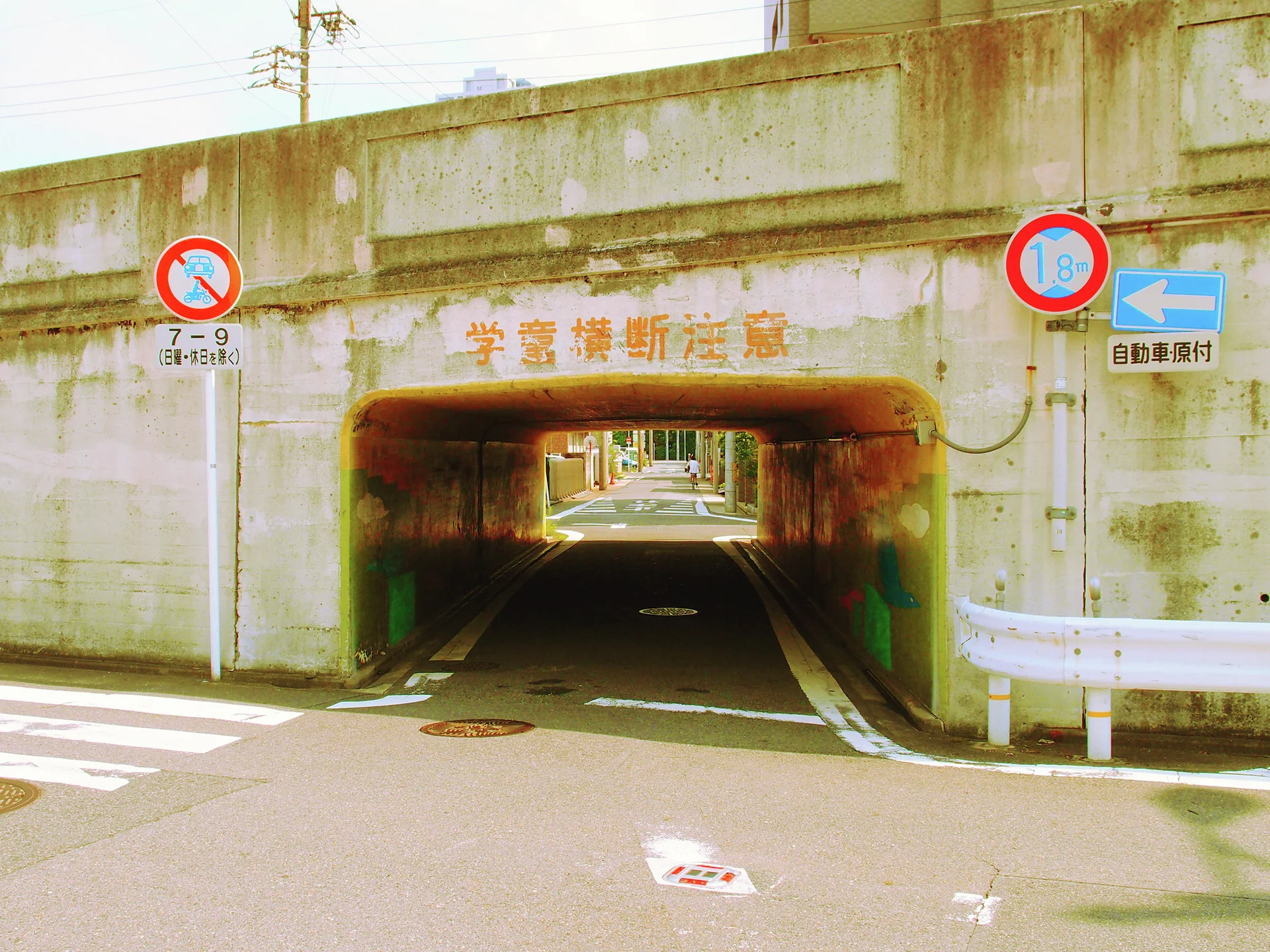 A low concrete underpass frames a narrow road beneath traffic restriction signs and stained walls.