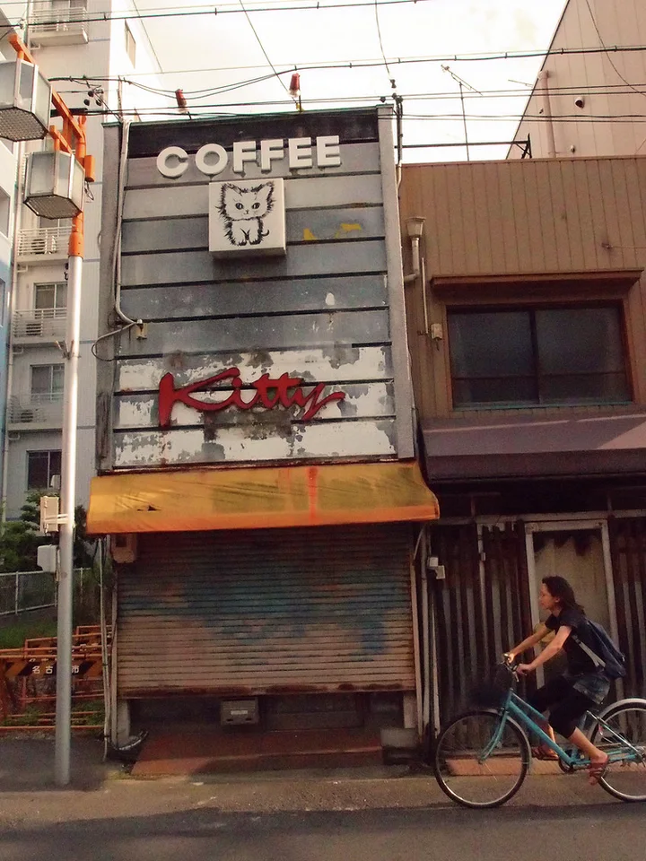 A cyclist passes a narrow closed coffee shop with a cat illustration above its awning.