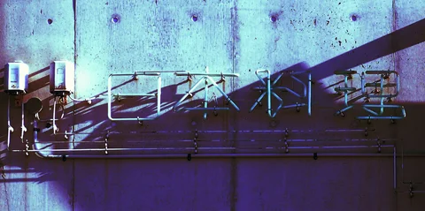 Thin metal Japanese characters stretch across a blue-toned concrete wall crossed by diagonal shadows.
