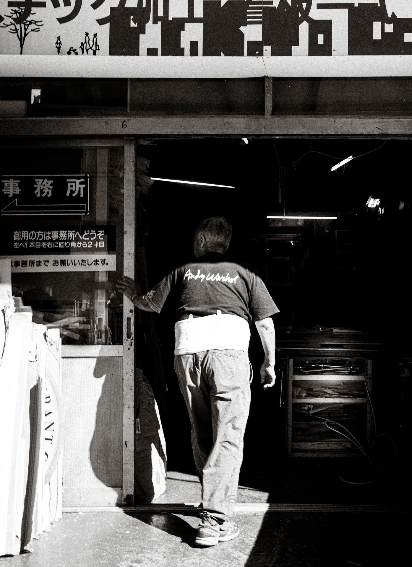 A person steps into a dark workshop beneath a large sign in black and white.