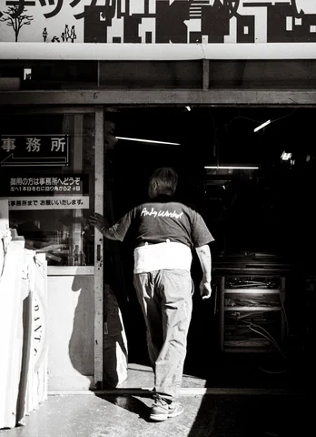 A person steps into a dark workshop beneath a large sign in black and white.