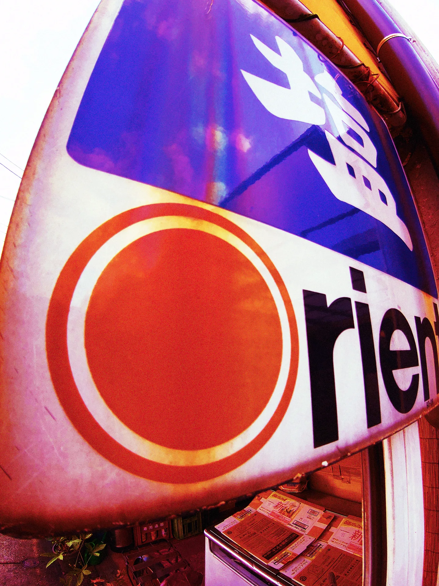 A curved shop sign displays a large red circle, dark lettering, and a purple panel.