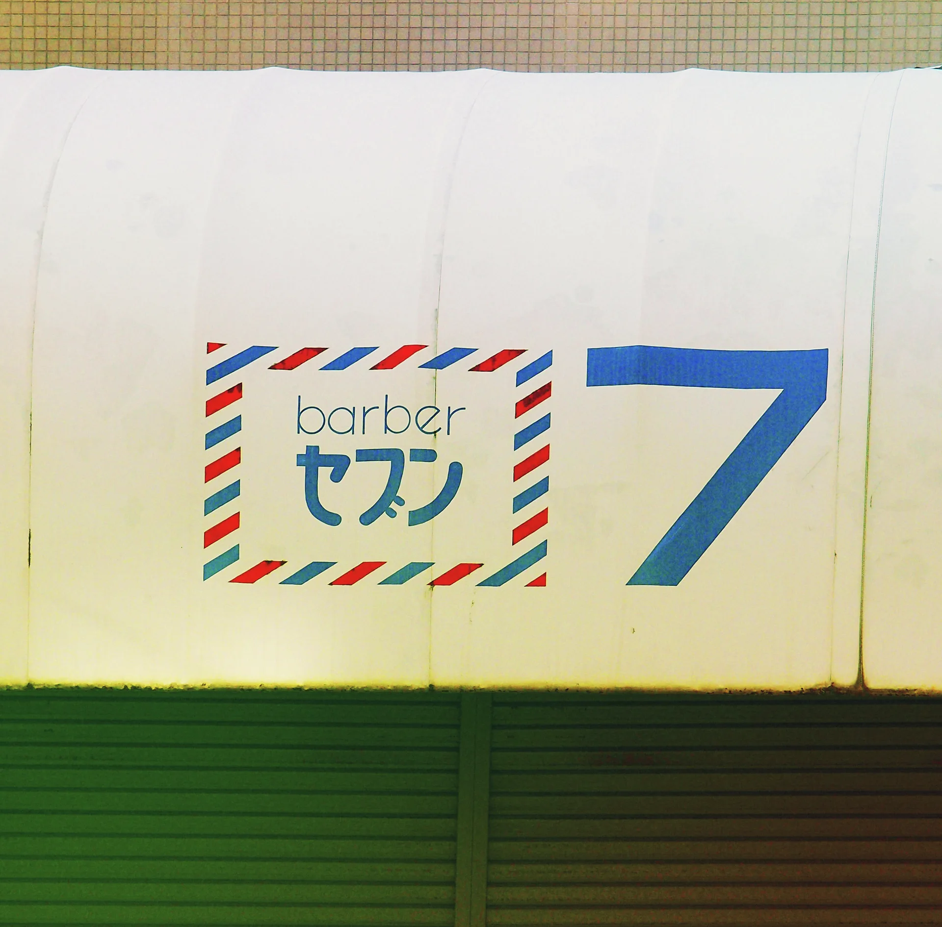 A small barber sign with striped borders sits beside a large blue numeral above closed shutters.