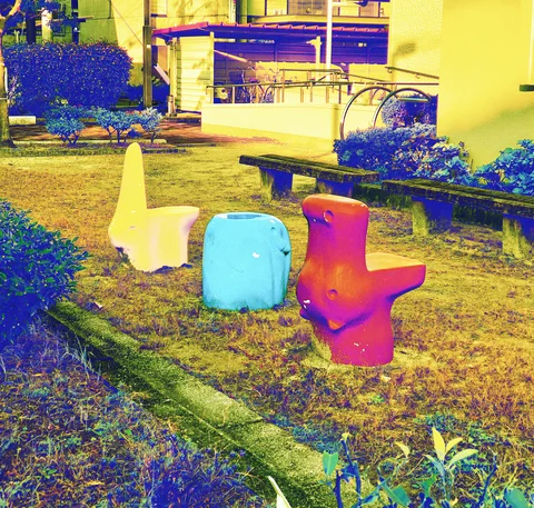 Three colorful molded play seats stand on grass beside low benches and shrubs.