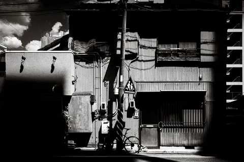 Sunlight falls on an old street facade with balcony railings and a parked bicycle in black and white.