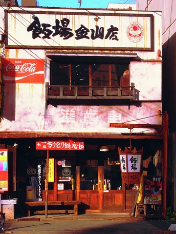 A pale restaurant facade has black Japanese signage above upper windows and a warmly lit wooden entrance.