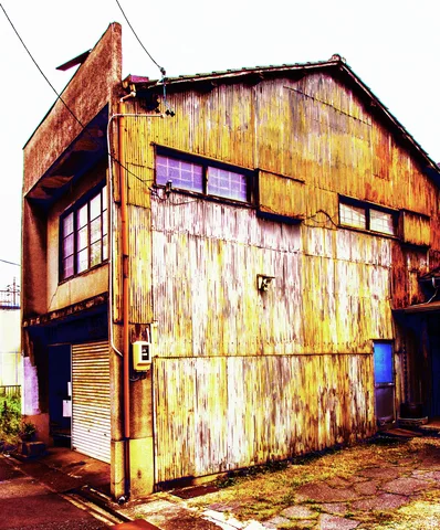 Heavy rust streaks cover a tall corrugated building with small windows and a closed corner shutter.