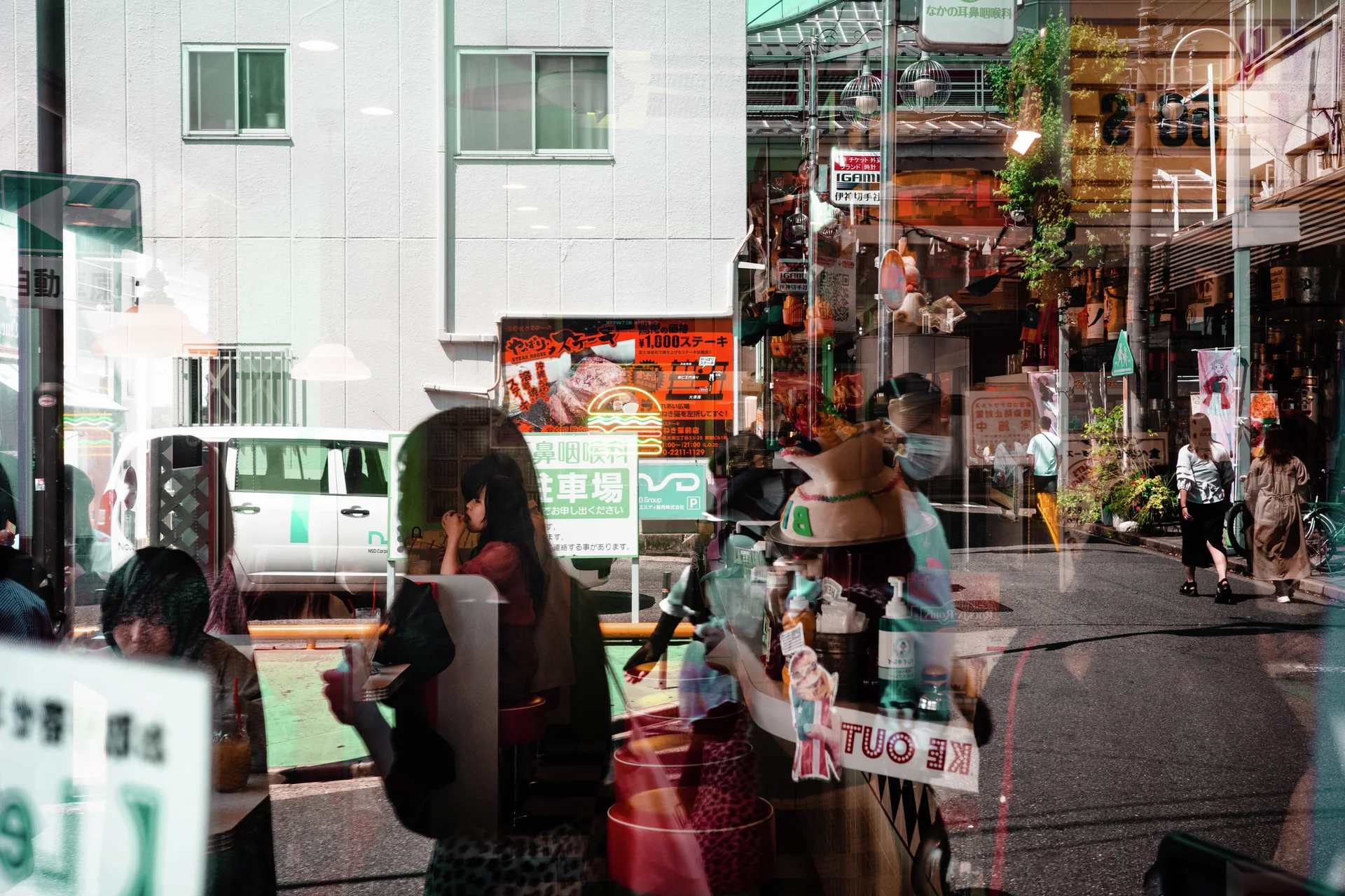 Reflected pedestrians overlap a street scene with a white van and buildings through a shop window.