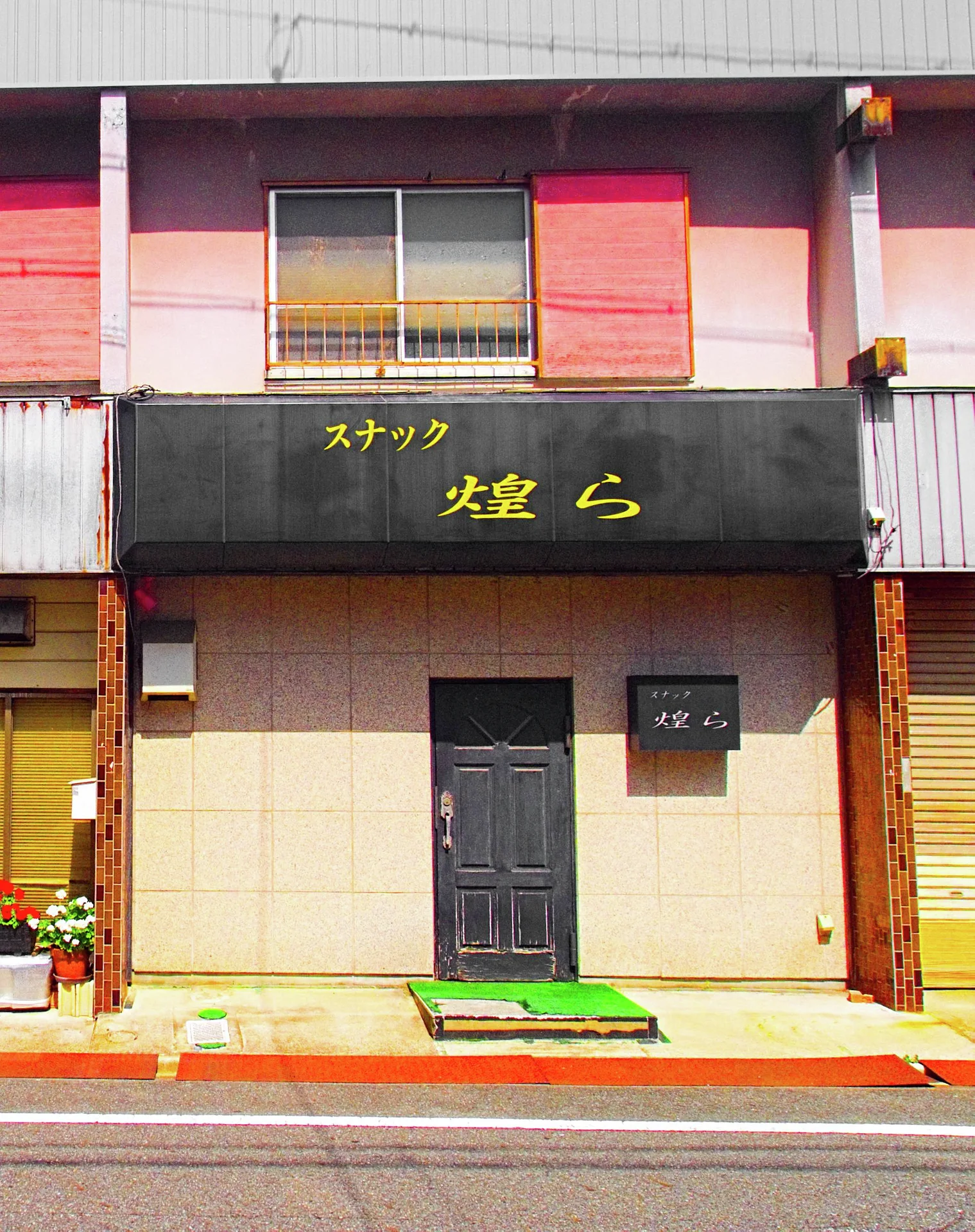 Gold Japanese lettering spans a black sign above a plain beige frontage and narrow dark door.