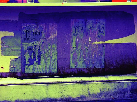 Torn faded notices cling to a purple-painted metal surface above a pale horizontal ledge.