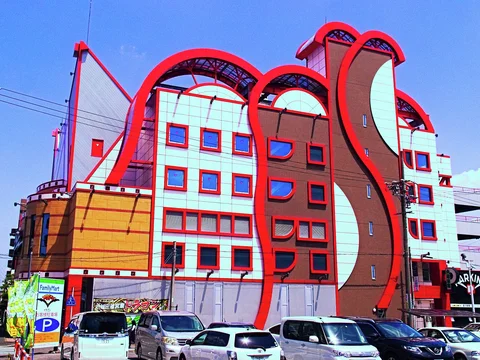 Curved red rooflines and a winding red facade rise above rows of parked cars.