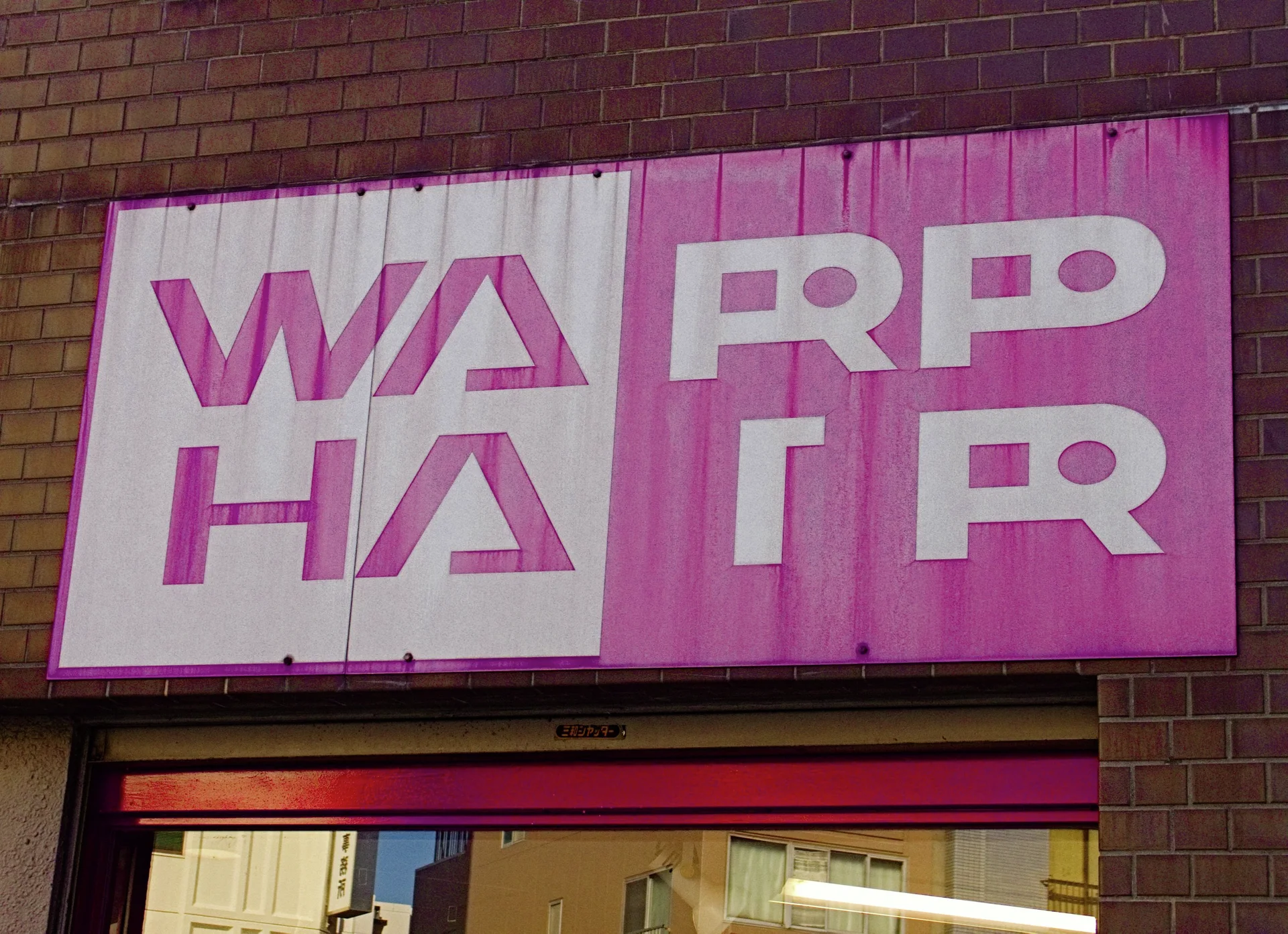 A weathered pink and white Warp Hair sign spans a brick storefront above a narrow entrance.