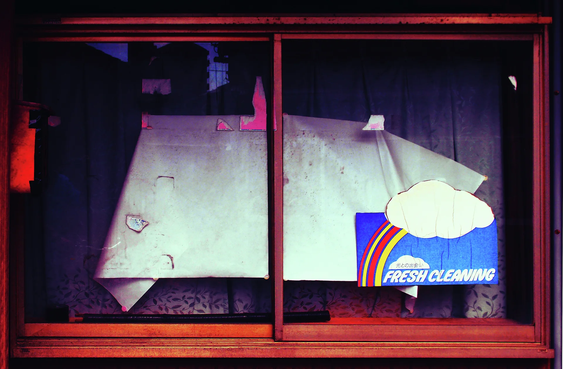 A rainbow-and-cloud Fresh Cleaning sticker sits on a dark window partly covered by torn pale paper.