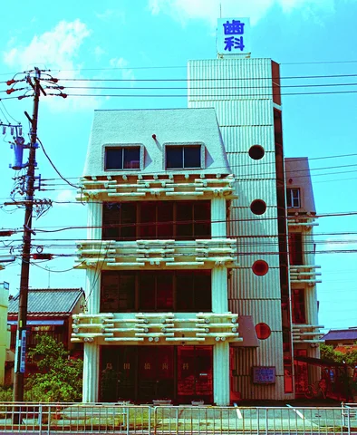 A narrow pale building combines decorative balcony rails and circular side windows behind overhead wires.