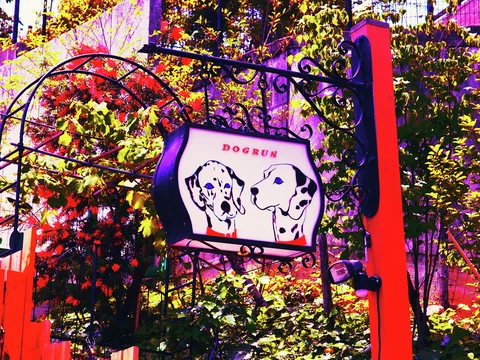 An illustrated dog sign hangs from decorative black metalwork between red posts and leafy plants.