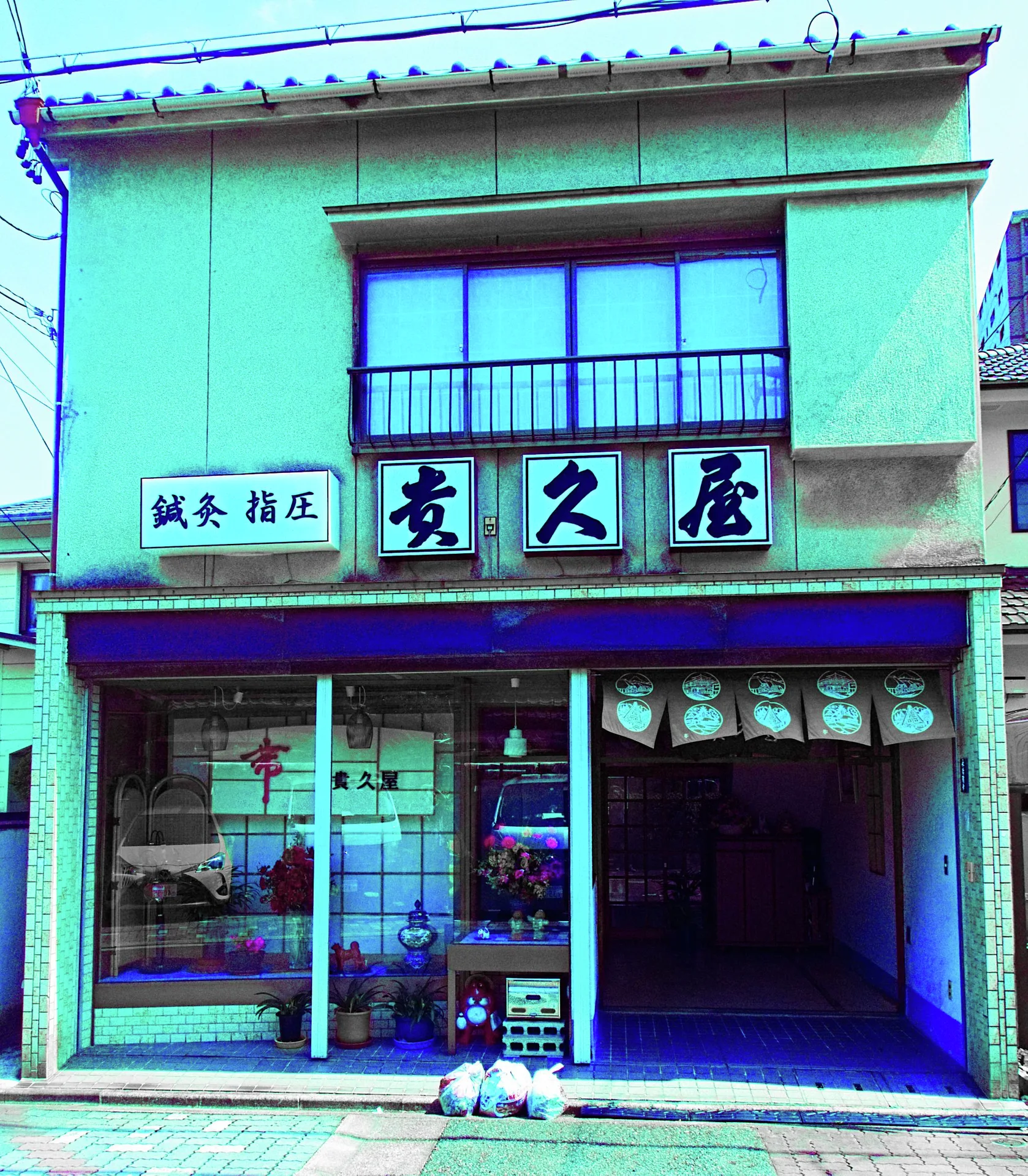 Black Japanese characters fill white sign panels beneath an upper window on a green-toned storefront.