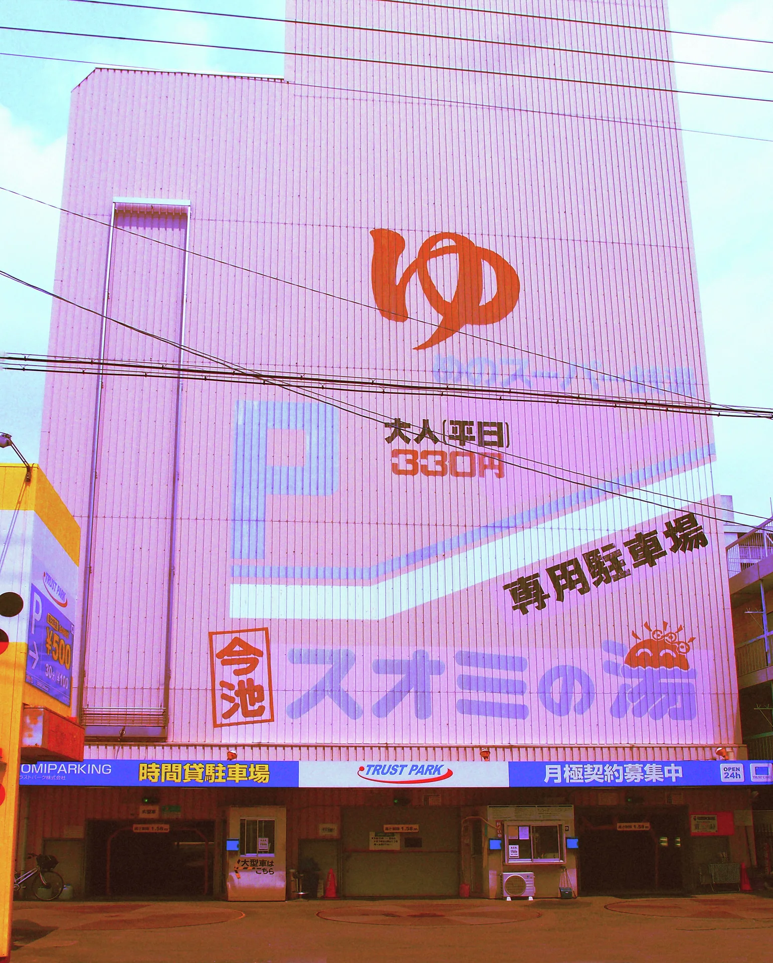 An orange symbol and large signs cover a pale building crossed by overhead utility wires.