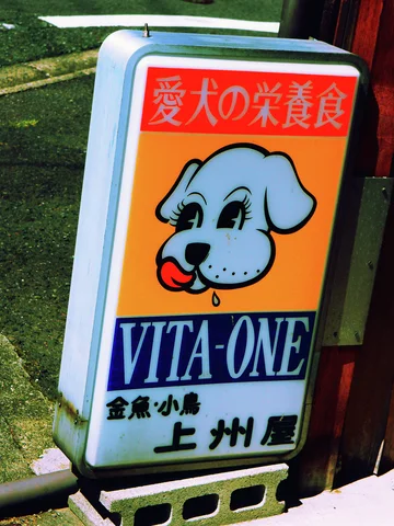 A dog illustration decorates an orange and white Vita-One sign beside a wooden post.