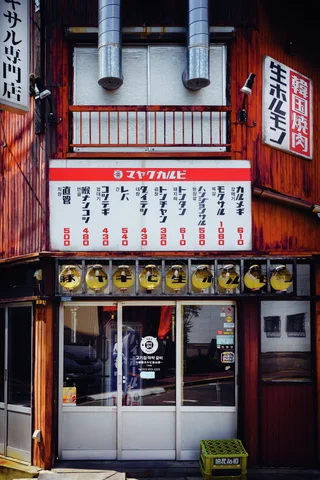 Two metal exhaust ducts descend above a restaurant entrance covered with Japanese menus and food illustrations.