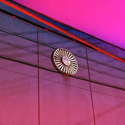 A circular radial emblem sits on a purple paneled wall beneath a vivid pink upper band.