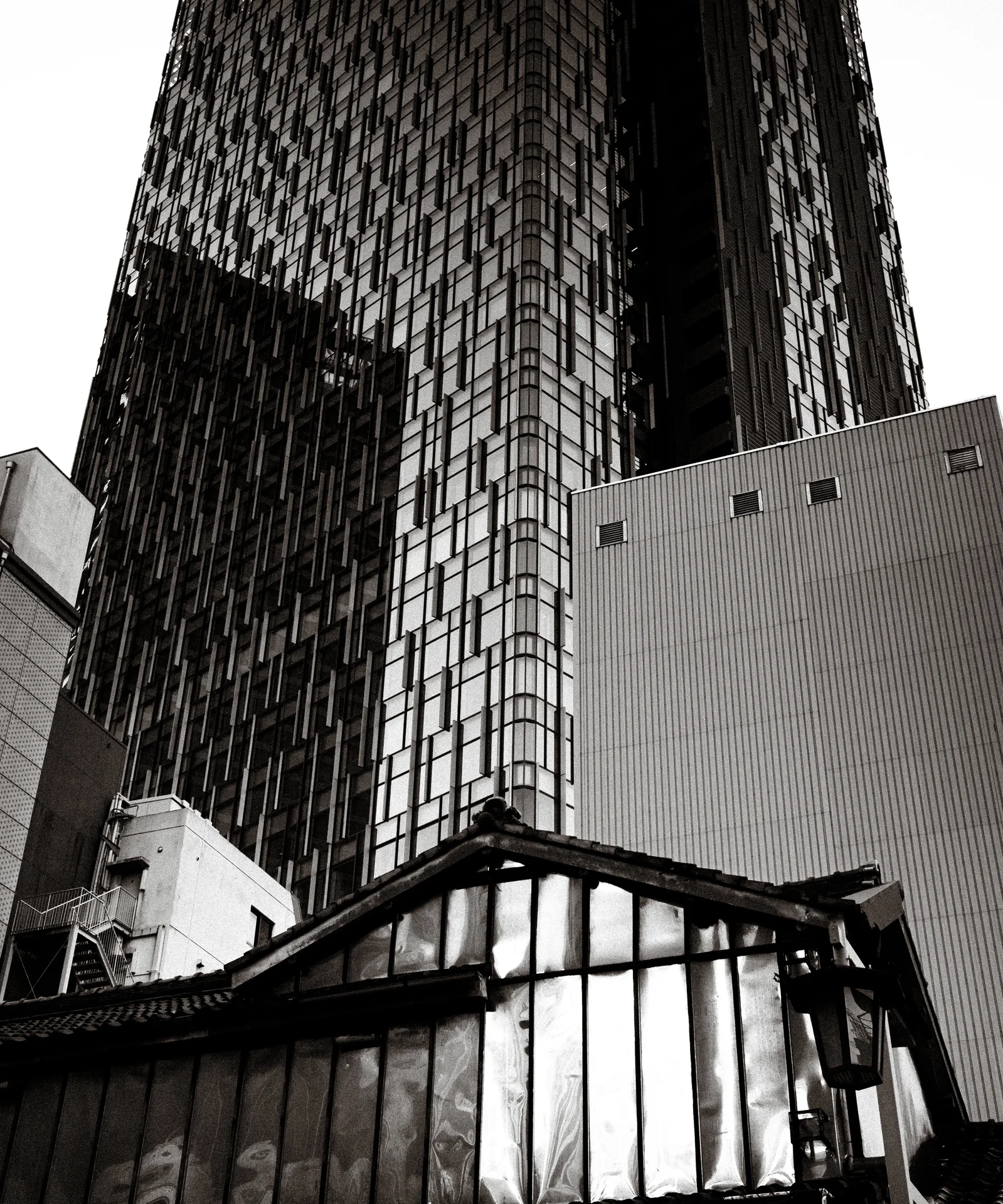 Tall patterned glass towers rise behind a small weathered gabled roof in black and white.