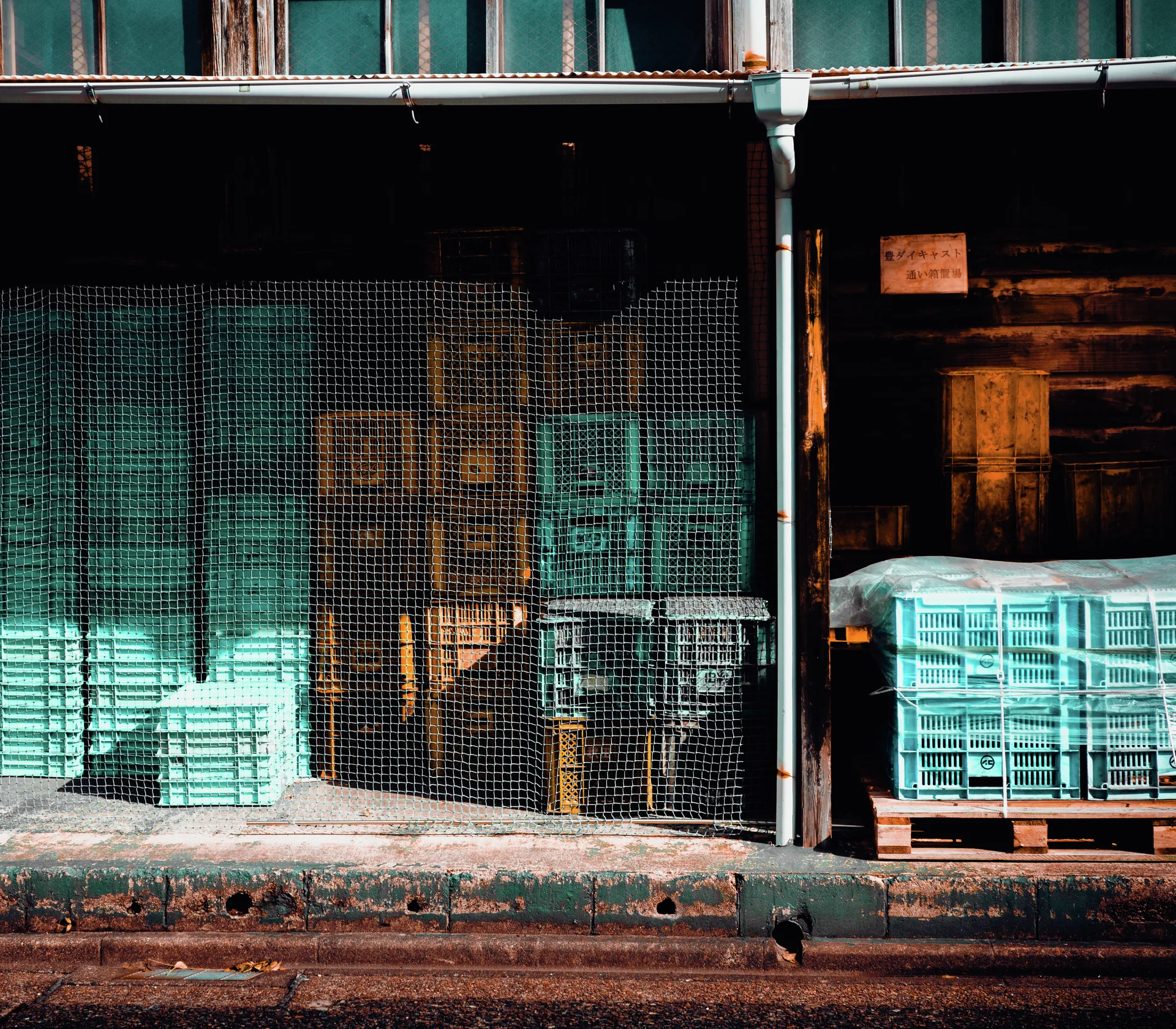 Turquoise plastic crates fill a dim storage frontage behind mesh screening and weathered wooden panels.