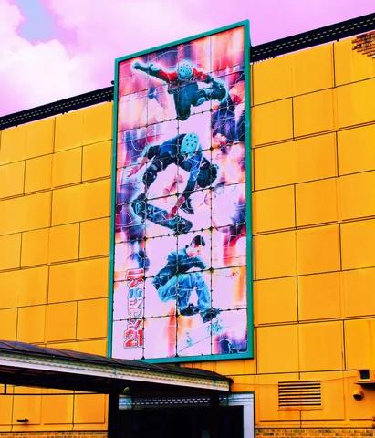 A tall colorful illustrated panel decorates a broad yellow building facade beneath pink clouds.