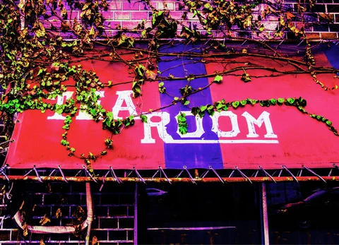 Trailing vines cross faded white lettering on a red and purple awning above dark cafe windows.
