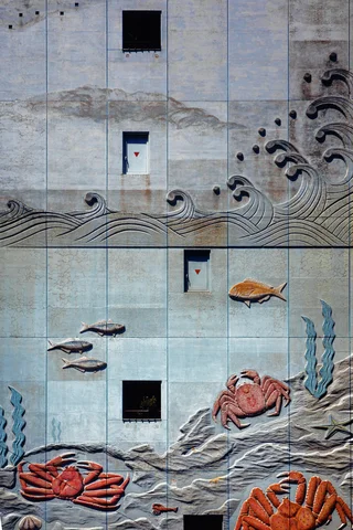 Sculpted waves, fish, and orange crabs decorate a pale tiled wall punctuated by small dark square openings.