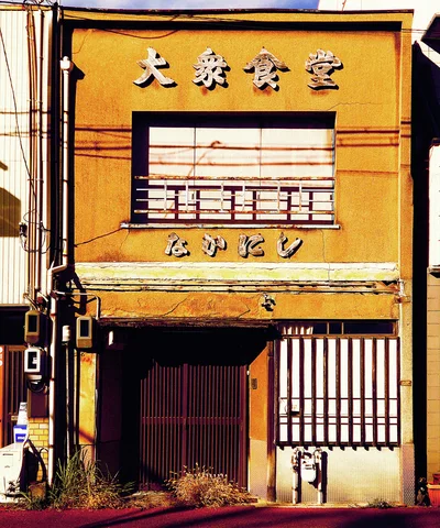 Raised pale characters decorate an ochre restaurant facade above a dark slatted entrance.