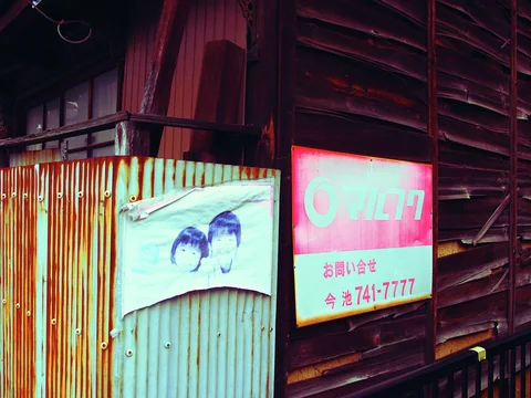 A faded notice and illustrated paper hang on weathered wooden siding beside a rust-streaked metal panel.