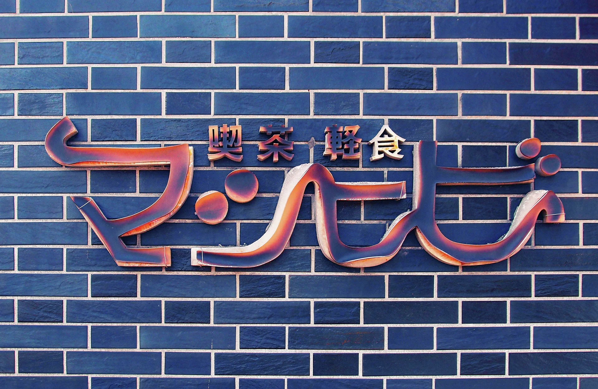 Curving raised reddish lettering decorates a wall covered in dark blue rectangular tiles.