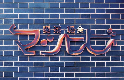 Curving raised reddish lettering decorates a wall covered in dark blue rectangular tiles.