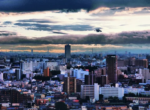 Dark layered clouds hang above a dense skyline of white buildings and scattered tall apartment blocks.