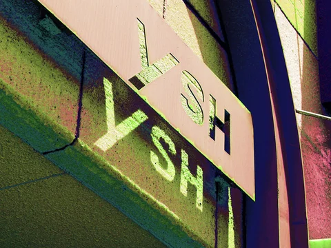 Cutout letters in a pale projecting panel cast sharp shadows across a green textured wall.