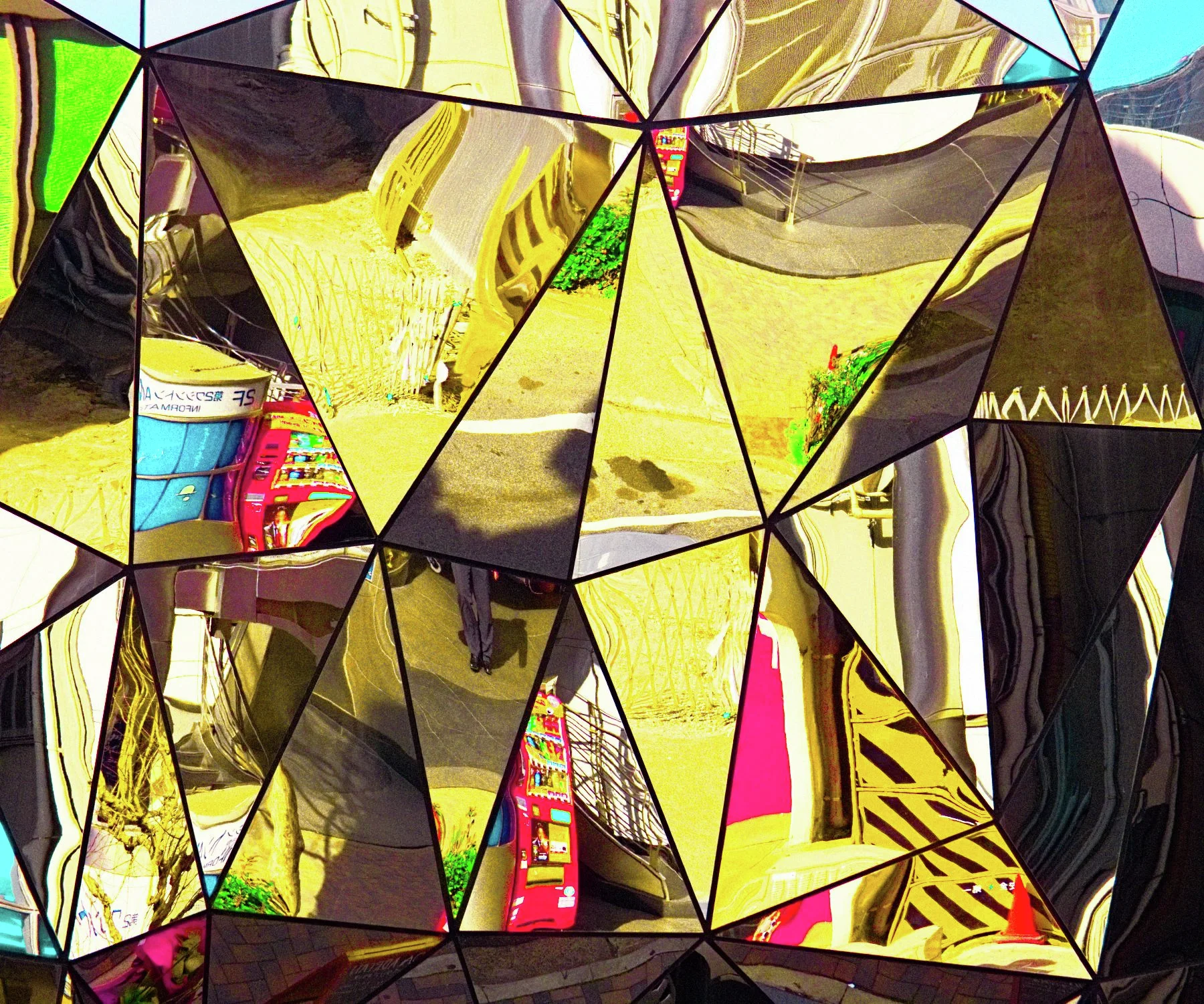 Triangular mirrored panels fragment yellow walls, colorful signs and nearby buildings into angular reflections.