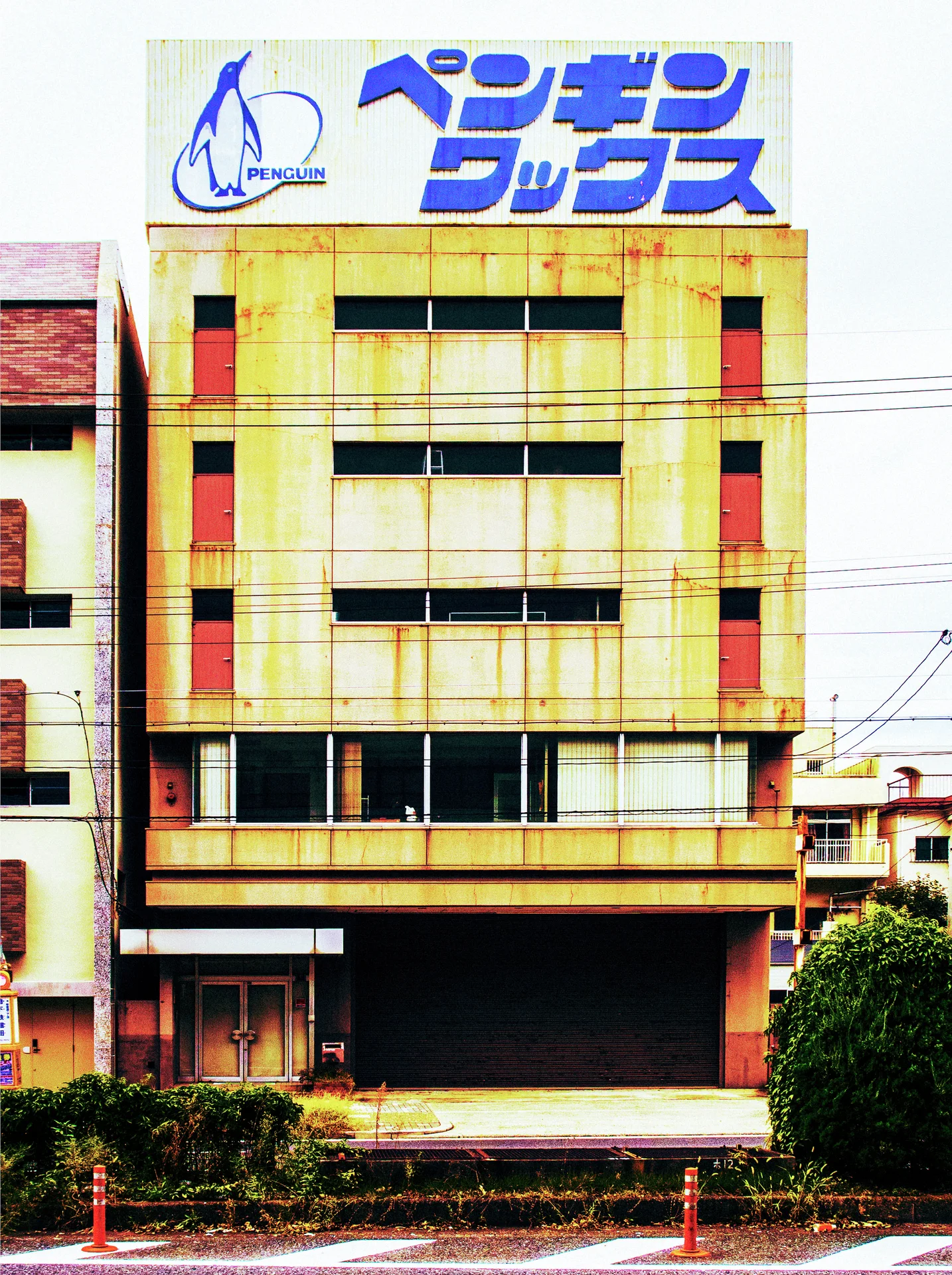 A tall yellow building has narrow horizontal windows and a large rooftop sign with a penguin graphic.