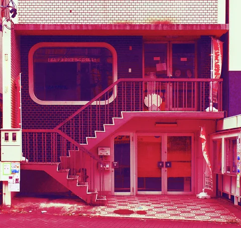 An exterior staircase crosses a red-tinted building facade above ground-level doors and a patterned tiled forecourt.