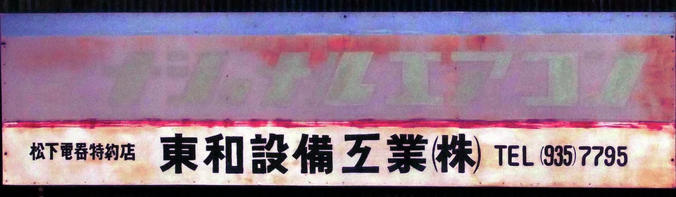 A long weathered pink sign sits above a pale panel with bold black Japanese lettering and a phone number.
