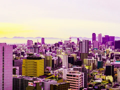 Dense purple-toned city buildings stretch toward distant hills beneath a pale sky with a yellow horizon.